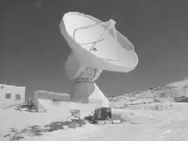 Description de l'image par IA : Antenne parabolique géante sur colline, bâtiments autour.