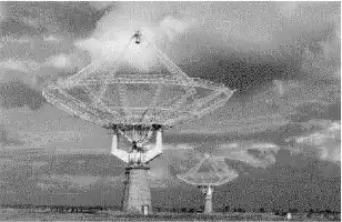 Description de l'image par IA : Deux grandes antennes paraboliques de 45 mètres de diamètre dans un champ sous un ciel nuageux.