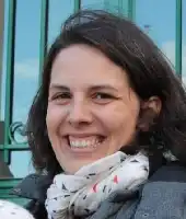 Description de l'image par IA : Femme souriante aux cheveux longs, portant un foulard à motifs, devant une rambarde verte.
