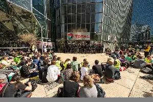 Description de l'image par IA : Manifestation devant le bâtiment Total, police en ligne face aux protestataires assis au sol.