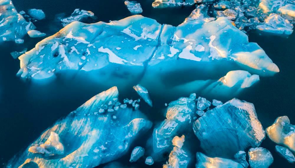 Description de l'image par IA : Des blocs de glace flottent dans une eau sombre, reflétant une lumière bleutée.