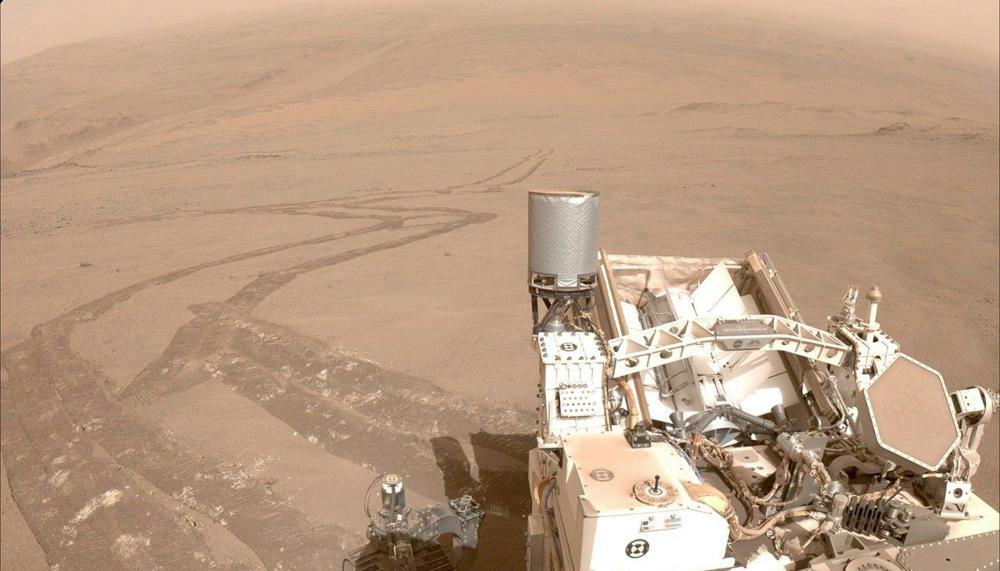 Description de l'image par IA : Rover Perseverance sur Mars, vue d'un paysage désertique avec des traces de roues et des instruments complexes.