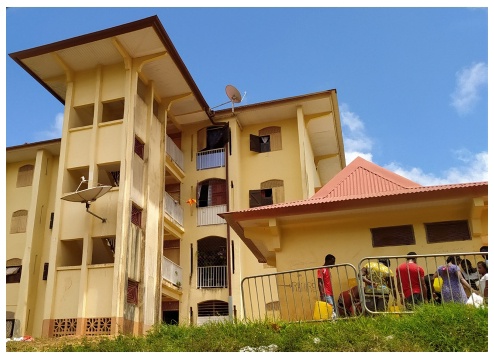 Description de l'image par IA : Bâtiment jaune avec balcon, toit rouge, personnes assises devant.