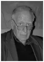 Description de l'image par IA : Homme âgé avec des lunettes, portant une veste sombre, sur fond neutre.